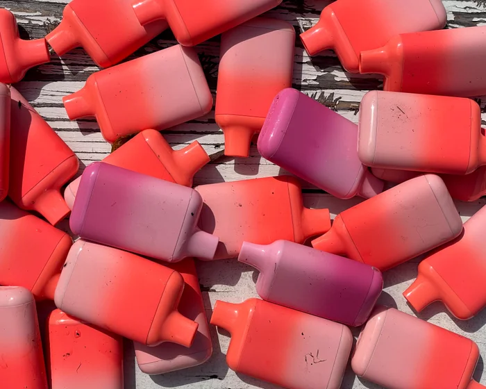 Discarded disposable vaping devices scattered on wooden boards