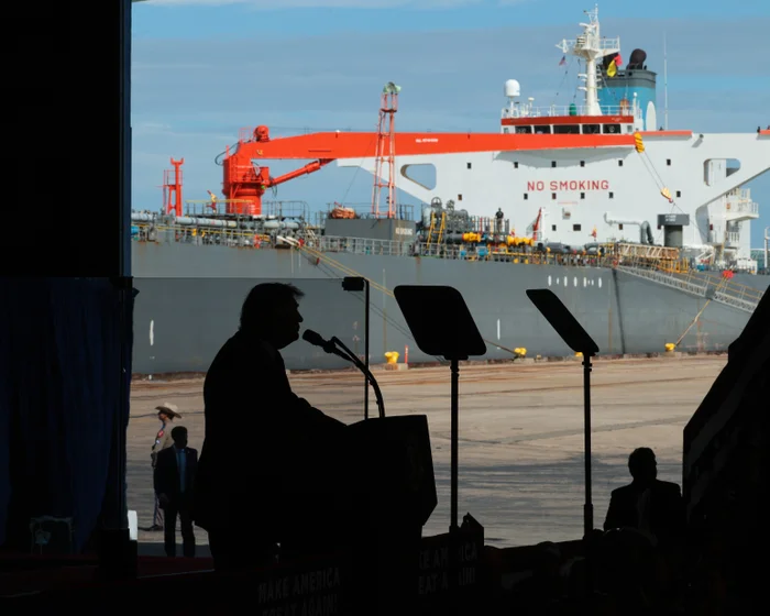 President Donald Trump stands at a podium in Corpus Christi, Texas, with a large oil tanker docked in the background during a campaign rally