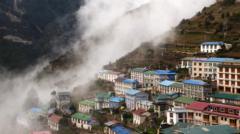 Buildings spread across terraced hillsides beneath Himalayan mountain peaks in Nepal