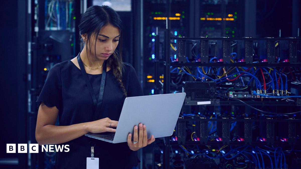 A technology worker using a laptop in a server room