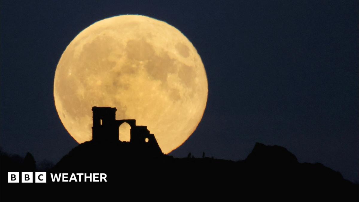 The full Hunter's Moon glowing with an amber hue low on the eastern horizon during an autumn evening