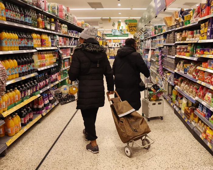 A shopper browsing price-labelled goods on a supermarket shelf in the United Kingdom