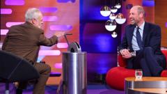 Prince William smiling while seated on the red sofa during a special episode of The Graham Norton Show.