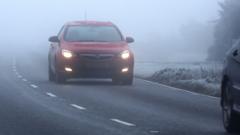 A highway shrouded in dense morning fog with vehicles navigating low visibility conditions.