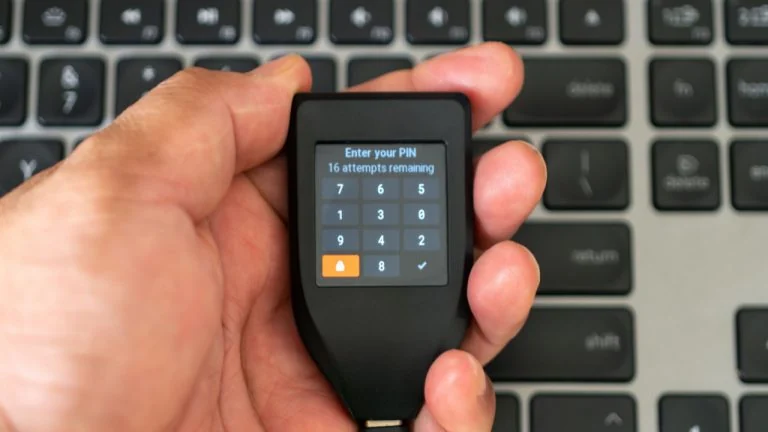 A Trezor hardware wallet resting on a surface alongside cybersecurity data visuals.