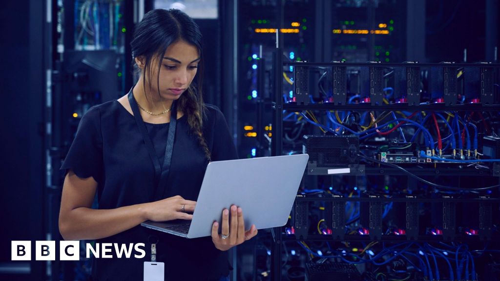 A technology worker using a laptop in a server room