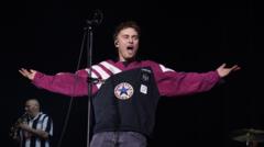 Sam Fender performing on stage wearing a Newcastle United shirt