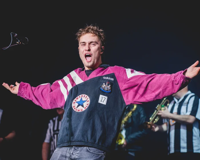 Sam Fender performing live on stage with an electric guitar at a large outdoor venue