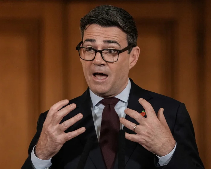 Andy Burnham gestures while speaking at a podium