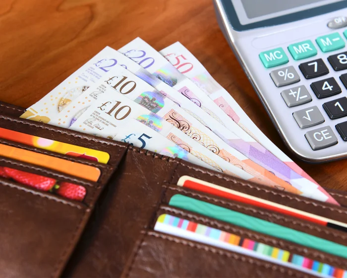 Pound notes and bank cards in a wallet beside a calculator