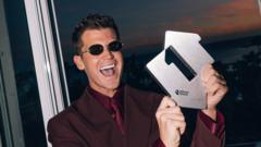 Jamie Miller smiles in a red suit and sunglasses while holding his UK number-one award.
