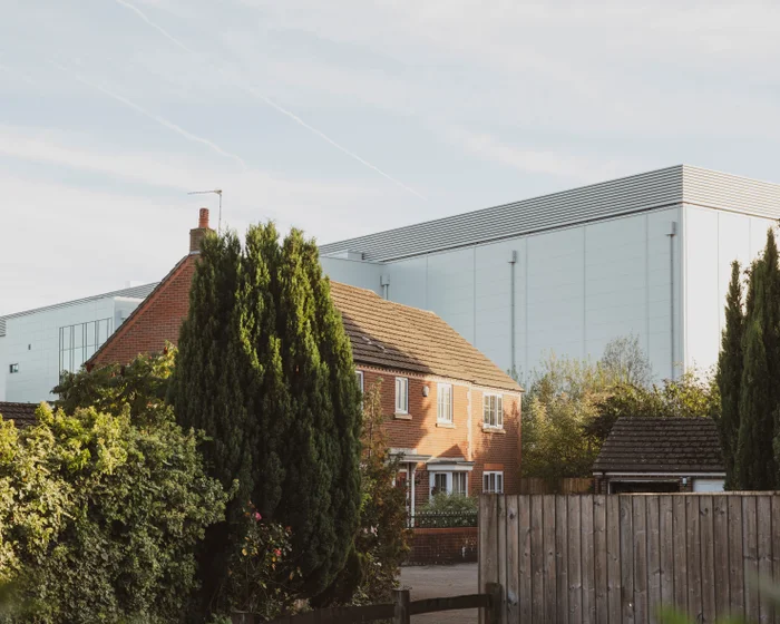 A large grey hyperscale datacentre building towering over suburban homes in Newport, South Wales, with a residential garden visible in the foreground