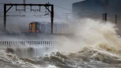Waves crashing against coastal defenses under dark storm clouds during high winds.